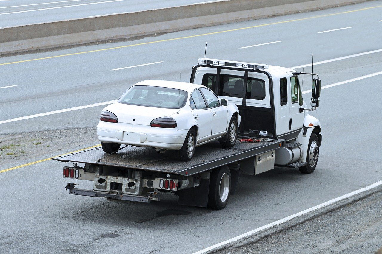 A white car is being towed by a tow truck.